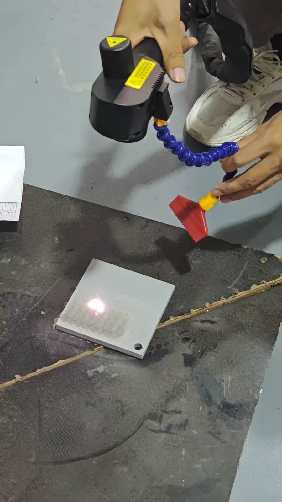 Handheld pulsed laser cleaning machine removing paint from galvanized sheet sample
